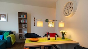Una sala de estar con una mesa de comedor, una estantería, un sofá y un reloj de pared.