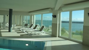 Zona de piscina con sillones de descanso y amplias ventanas con vista al mar.