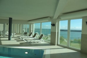 Area piscina con lettini e ampie finestre vista mare.