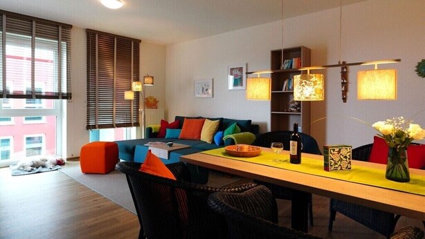 Un salón moderno con sofá, mesa de comedor, sillas, estantería y ventana con persianas.