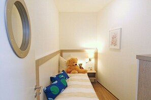 Une petite pièce accueillante, avec un lit, une table de chevet, un ours en peluche et un miroir fixé au mur.