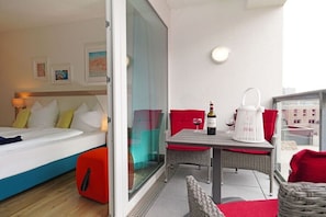 Una camera d'albergo con un letto, un tavolo con bottiglia e bicchiere, e un balcone con mobili in vimini.