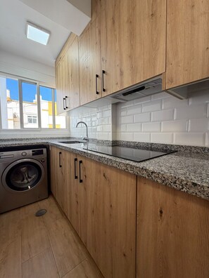 A kitchen with wooden cabinets, a stainless steel sink, and a built-in washing machine. - Terrasol Jupiter, 9th Floor (Torre del Mar)