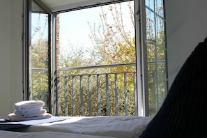 A room with a bed, a window with a view of trees, and a stack of towels on the windowsill. - Bernstein Suite & Breakfast Apartment 04 (Büum)