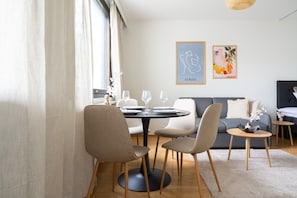 A modern dining area with a round table, chairs, and a sofa. There are framed artworks on the wall and a window with curtains. - Nordic City Studio By Lapland Host (Rovaniemi)