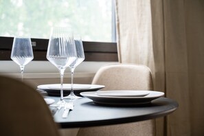 A dining table with two wine glasses and plates, set against a window with curtains.