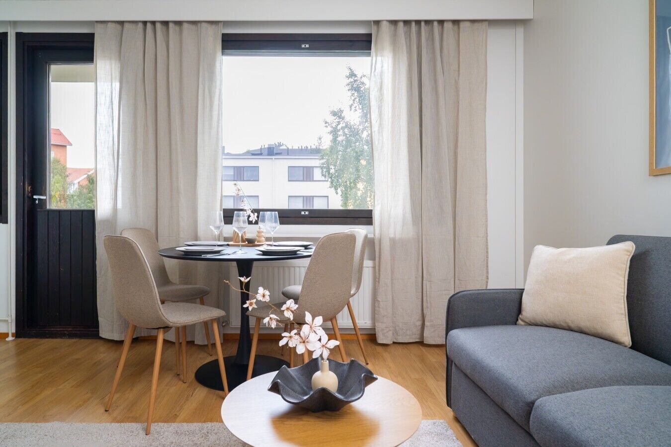 Un salon moderne avec un canapé gris, une table à manger avec des chaises et une fenêtre avec des rideaux.