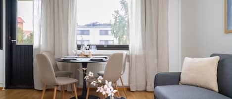 A modern living room with a grey sofa, a dining table with chairs, and a window with curtains.