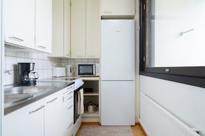 A compact kitchen with white cabinets, a stainless steel sink, a coffee maker, a microwave, and a refrigerator. - Nordic City Studio By Lapland Host (Rovaniemi)