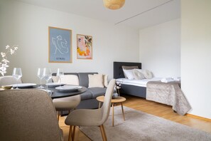 Ein modernes Hotelzimmer mit Essecke, einem Bett mit dunklem Kopfteil und zwei gerahmten Kunstwerken an der Wand.