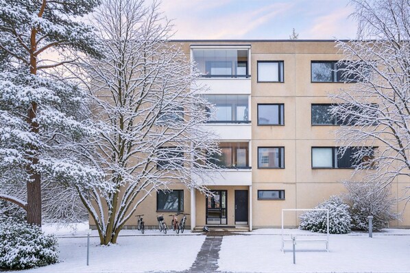 A multi-story building with a snow-covered exterior, a visible entrance, and a bicycle parked outside.