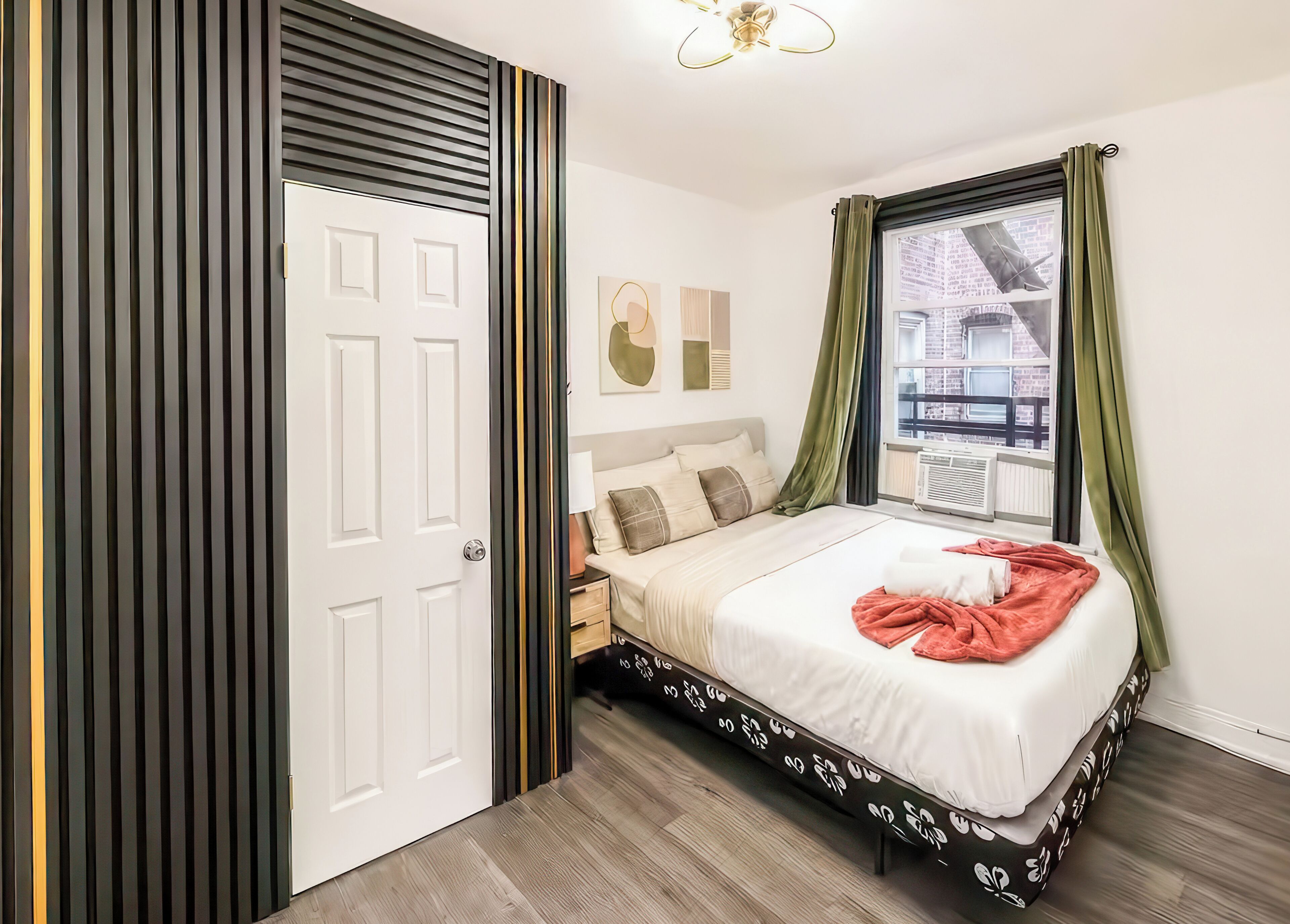 A bedroom with a bed, a nightstand, a window with curtains, and a door with a striped design.