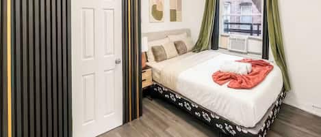 Un dormitorio con una cama, una mesita de noche, una ventana con cortinas y una puerta con diseño a rayas.