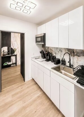 A modern kitchen with white cabinets, a stainless steel sink, and a black microwave. - 20 Mins to Times Square Skyline Views (West New York)