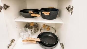 A kitchen cabinet with three black frying pans and a measuring cup.