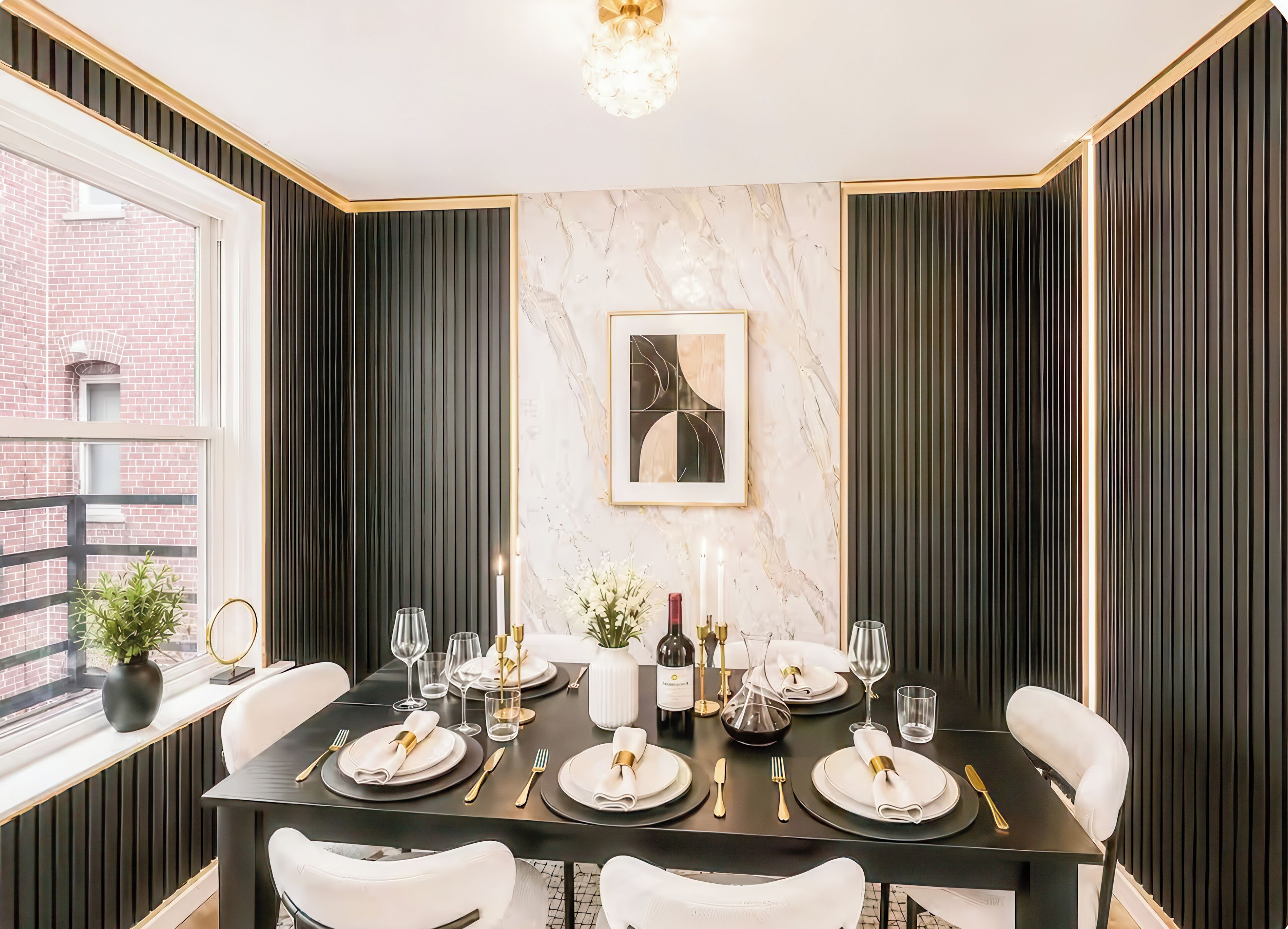 Un coin repas avec une table noire dressée pour six personnes, des chaises blanches et un mur en marbre orné d’une œuvre d’art encadrée.