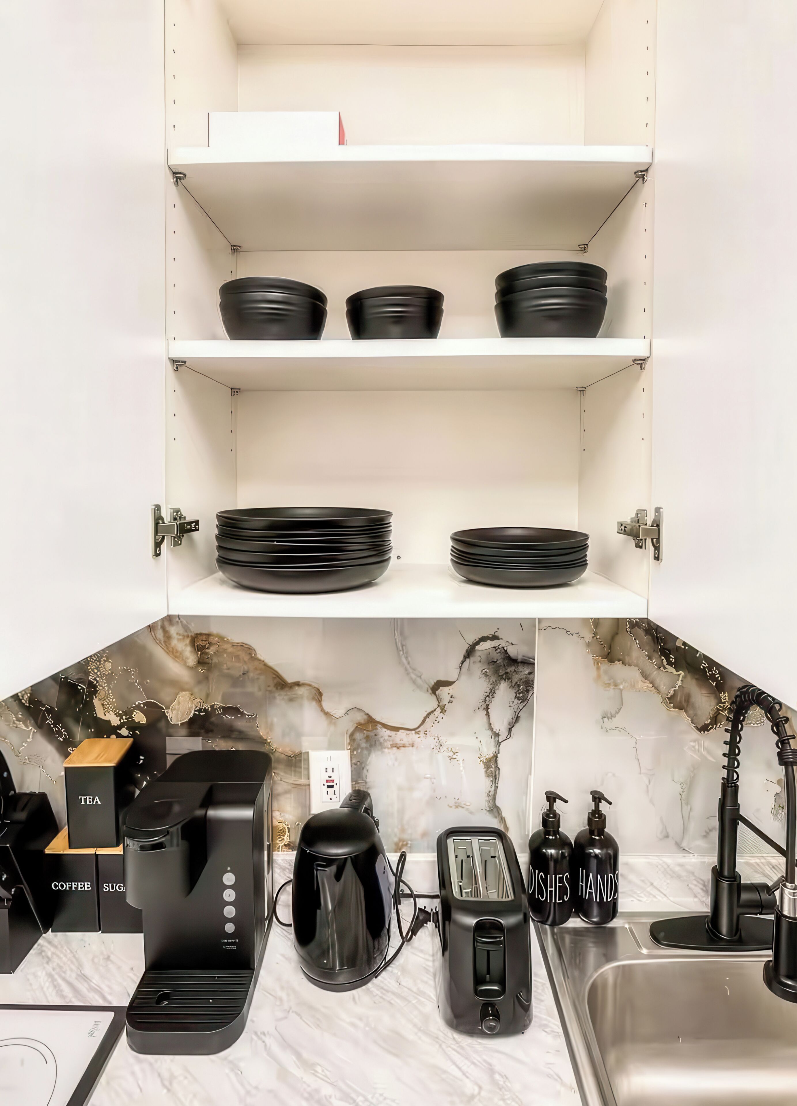 Une cuisine avec des meubles blancs, des appareils électroménagers noirs et un dosseret en marbre.