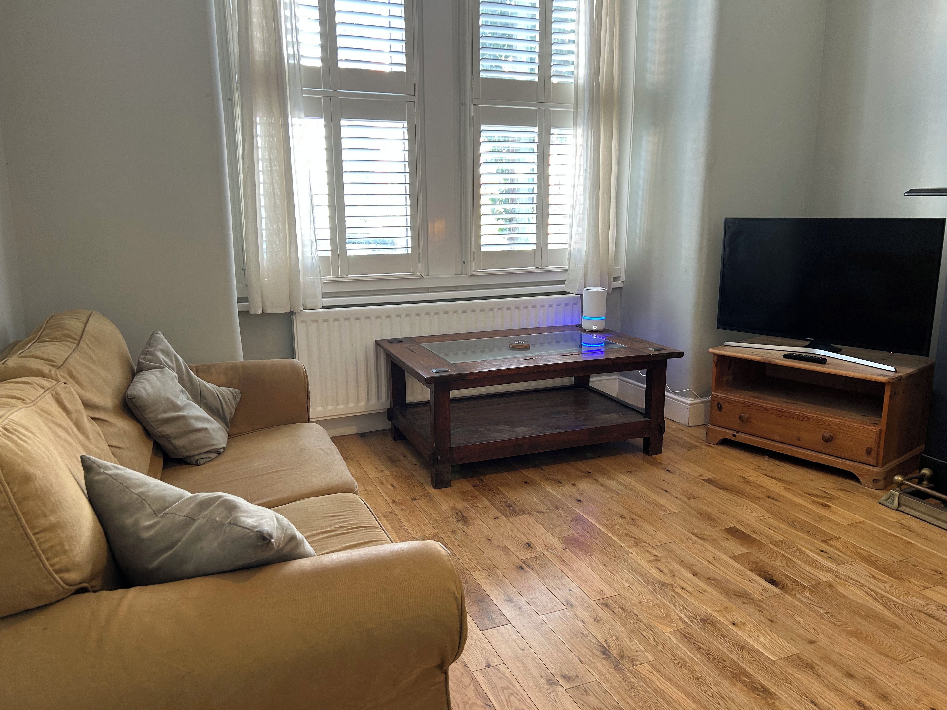 A living room with a sofa, a coffee table, a TV stand, and a window with blinds.