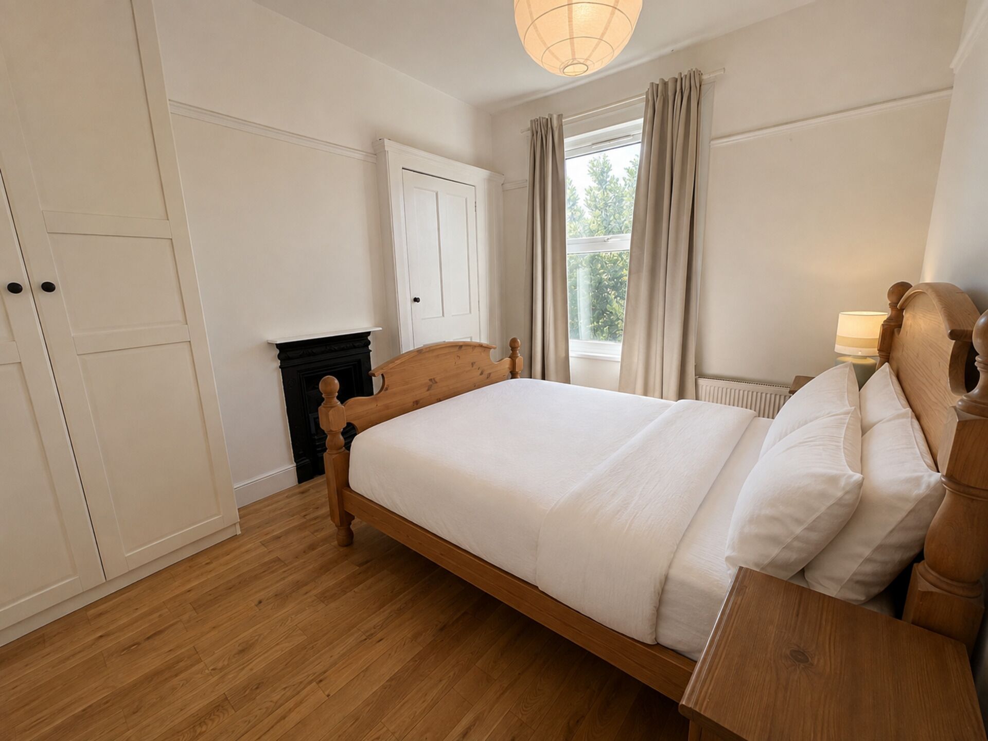 A bedroom with a wooden bed, a nightstand, a fireplace, and a window with curtains.