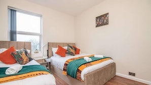 Et hotelværelse med to senge, et vindue, et billede på væggen og et natbord med en lampe.
