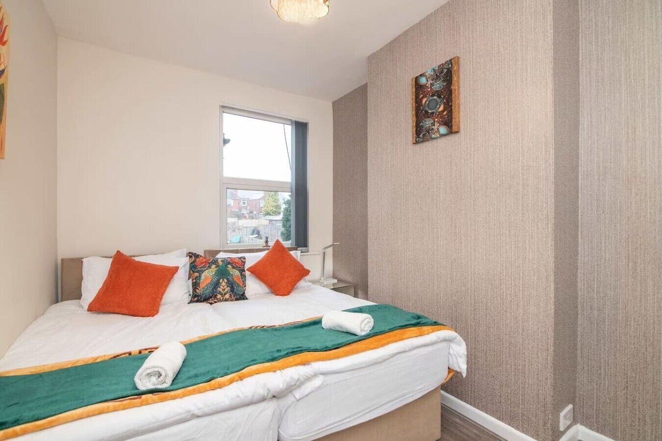 Ein Hotelzimmer mit einem Bett, Kissen, einem Fenster und einem an der Wand hängenden Kunstwerk.