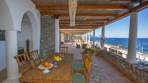 Un área de comedor al aire libre con una mesa dispuesta para dos, rodeada de pilares de piedra y vista al mar.