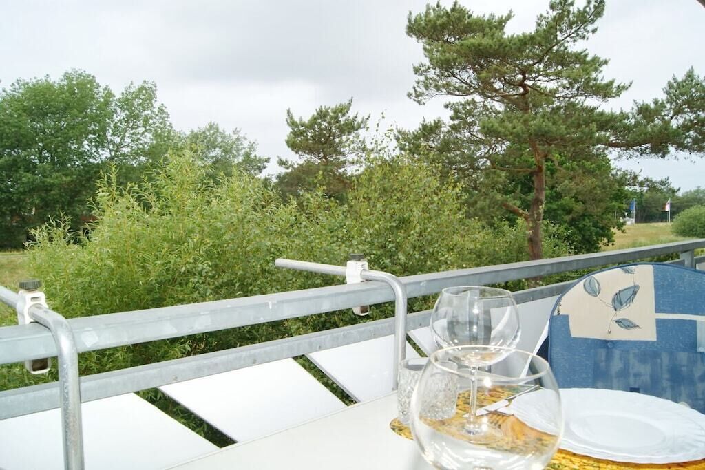 A table with a metal railing, a glass of water, and a plate on a table outdoors with trees in the background.