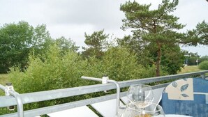Ulkokäytössä oleva pöytä, jossa on metallinen reunakaide, lasi vettä ja lautanen. Taustalla näkyy puita.