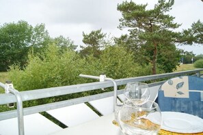 Ein Tisch mit Metallgeländer, einem Glas Wasser und einem Teller im Freien, mit Bäumen im Hintergrund.