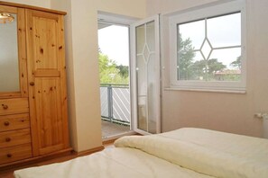Ein Schlafzimmer mit einem Holzschrank, einem Bett mit weißer Daunendecke und einem Fenster mit Blick ins Freie.