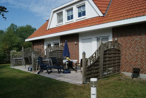 Ein Wohngebäude mit Backsteinfassade, rotem Ziegeldach und einer überdachten Veranda mit Gartenmöbeln.