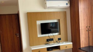 A room with a built-in TV, wooden cabinets, and an air conditioning unit. - KOKO Regency Hotel & Hospitality (Gandhinagar)