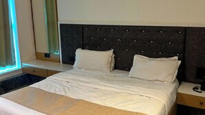 A hotel room with a large bed, a bedside table, and a mirror. - KOKO Regency Hotel & Hospitality (Gandhinagar)