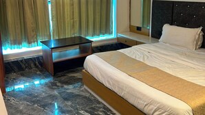 A hotel room with a large bed, a nightstand, a mirror, and a window with curtains. - KOKO Regency Hotel & Hospitality (Gandhinagar)