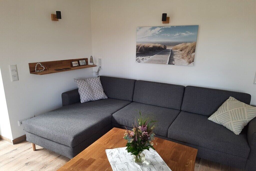A modern living room with a grey sectional sofa, a wooden coffee table with a floral centerpiece, a wall-mounted shelf with decorative items, and a beach-themed painting.