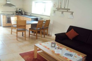 A modern kitchen with a dining area, a black sofa, and a coffee table with magazines. - Holiday home with 1 bedroom (Mettlach-Tünsdorf)