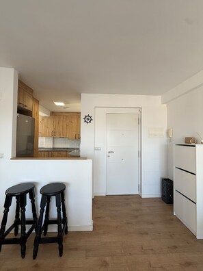 A kitchen with wooden cabinets, a white door, and two black stools. - Terrasol J Piter 9 Planta (Velez-Malaga)