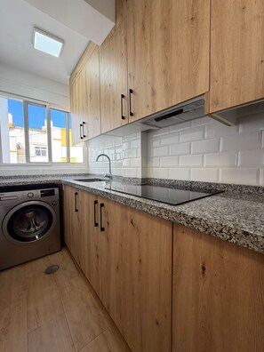 A kitchen with wooden cabinets, a stainless steel sink, and a built-in washing machine. - Terrasol J Piter 9 Planta (Velez-Malaga)