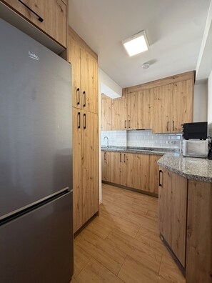 A modern kitchen with wooden cabinets, a stainless steel refrigerator, and a microwave on the countertop. - Terrasol J Piter 9 Planta (Velez-Malaga)