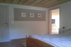 Un dormitorio con una cama de madera, una puerta blanca y un televisor montado en la pared.