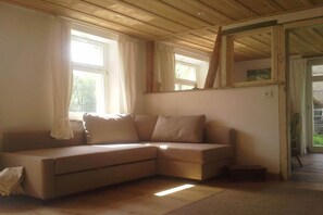 Ein Zimmer mit einem beigen Sofa, einem kleinen Tisch und einem Fenster mit Vorhängen.