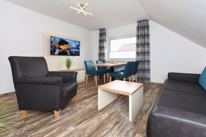 A modern living room with a television, a dining area with chairs, and a sofa. - Holiday apartments "Seagull 3" (Esens-Bensersiel)