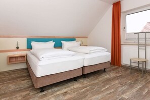 A double bed with white linens in a room with wooden flooring, a teal headboard, and a window with orange curtains. - Holiday apartments "Seagull 3" (Esens-Bensersiel)