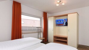 Ett hotellrum med två sängar, en tv, ett fönster med gardiner och ett element.