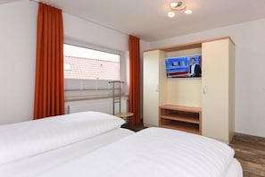 Habitación de hotel con dos camas, televisión, ventana con cortinas y radiador.
