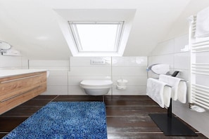 Un baño moderno con tragaluz, tocador de madera, felpudo negro y toallero.