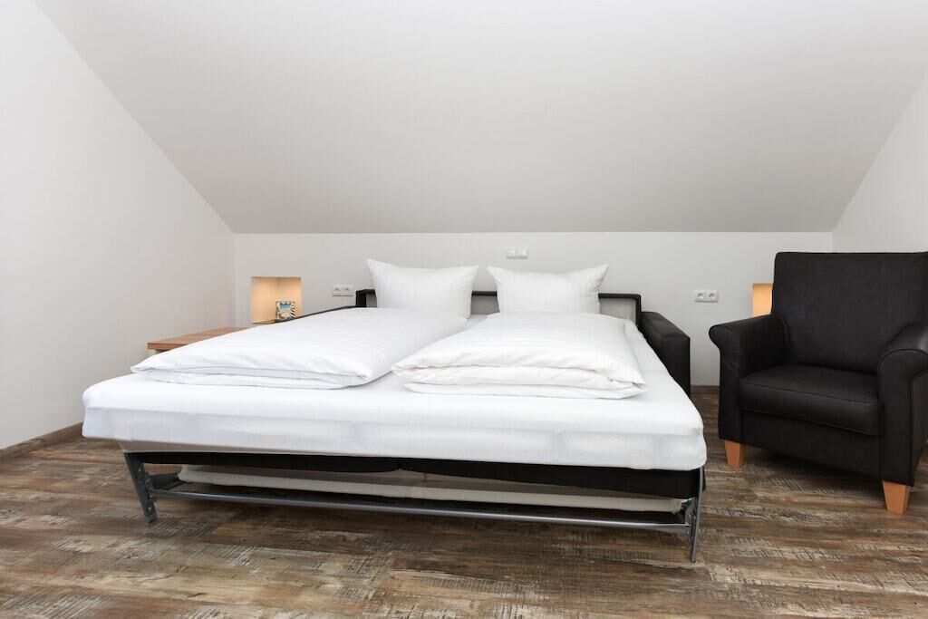 Ein Einzelbett mit weißer Bettwäsche in einem Zimmer mit schrägem Dach.