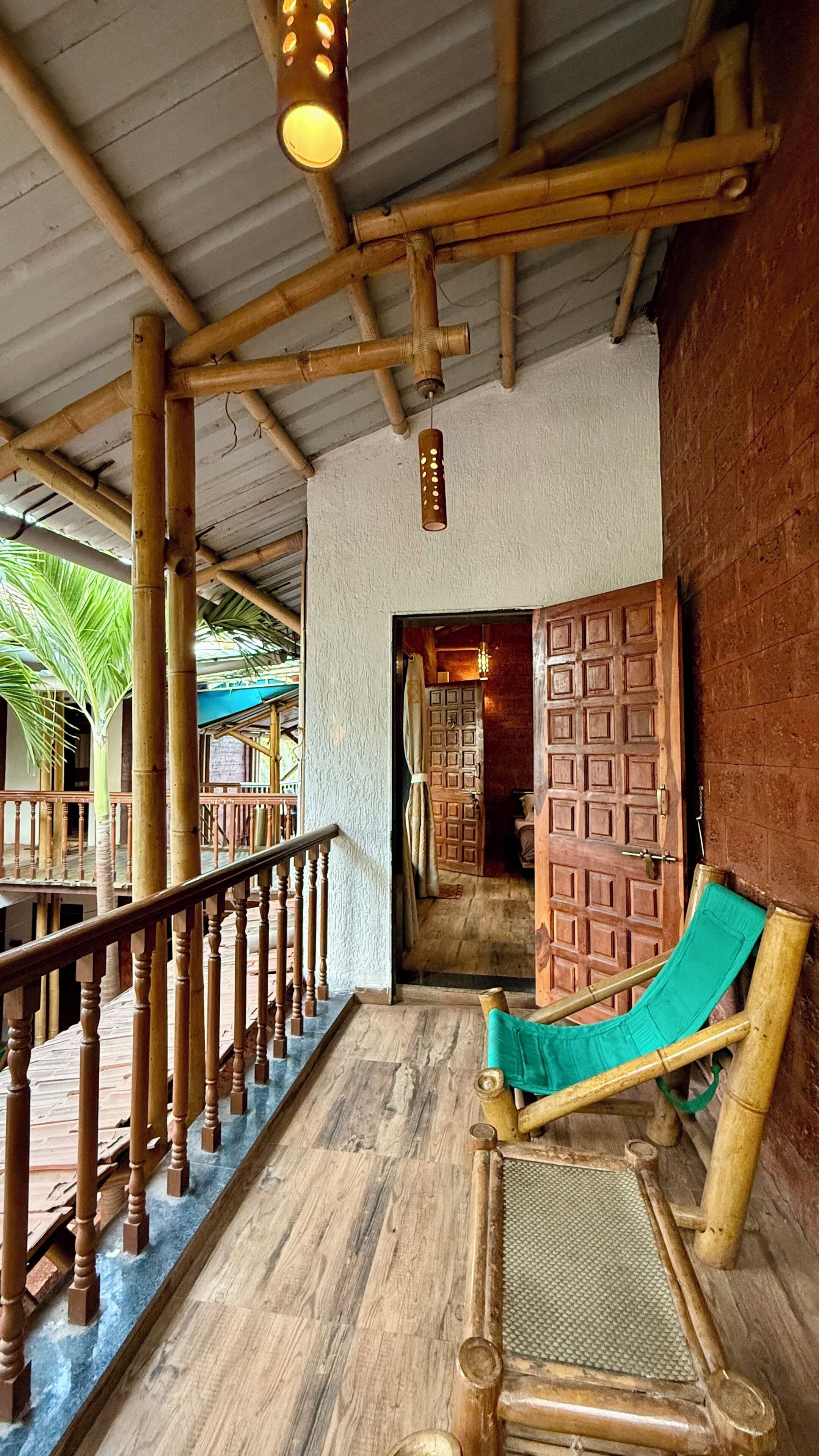 Una escalera de madera conduce a un espacio cubierto con una silla de lounge verde y un techo de bambú.