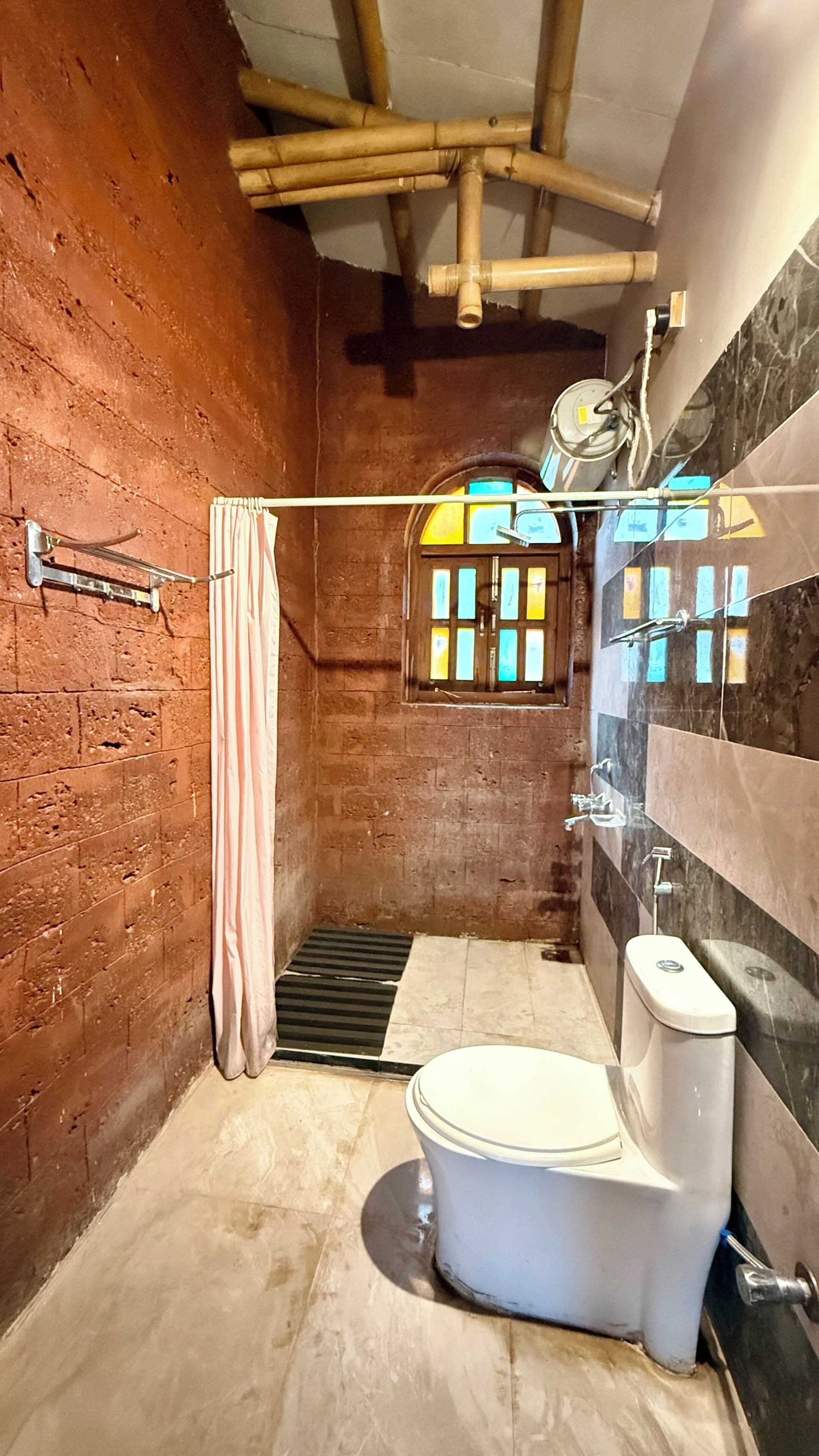 Un baño pequeño y cerrado con inodoro, ducha y una ventana con barrotes.