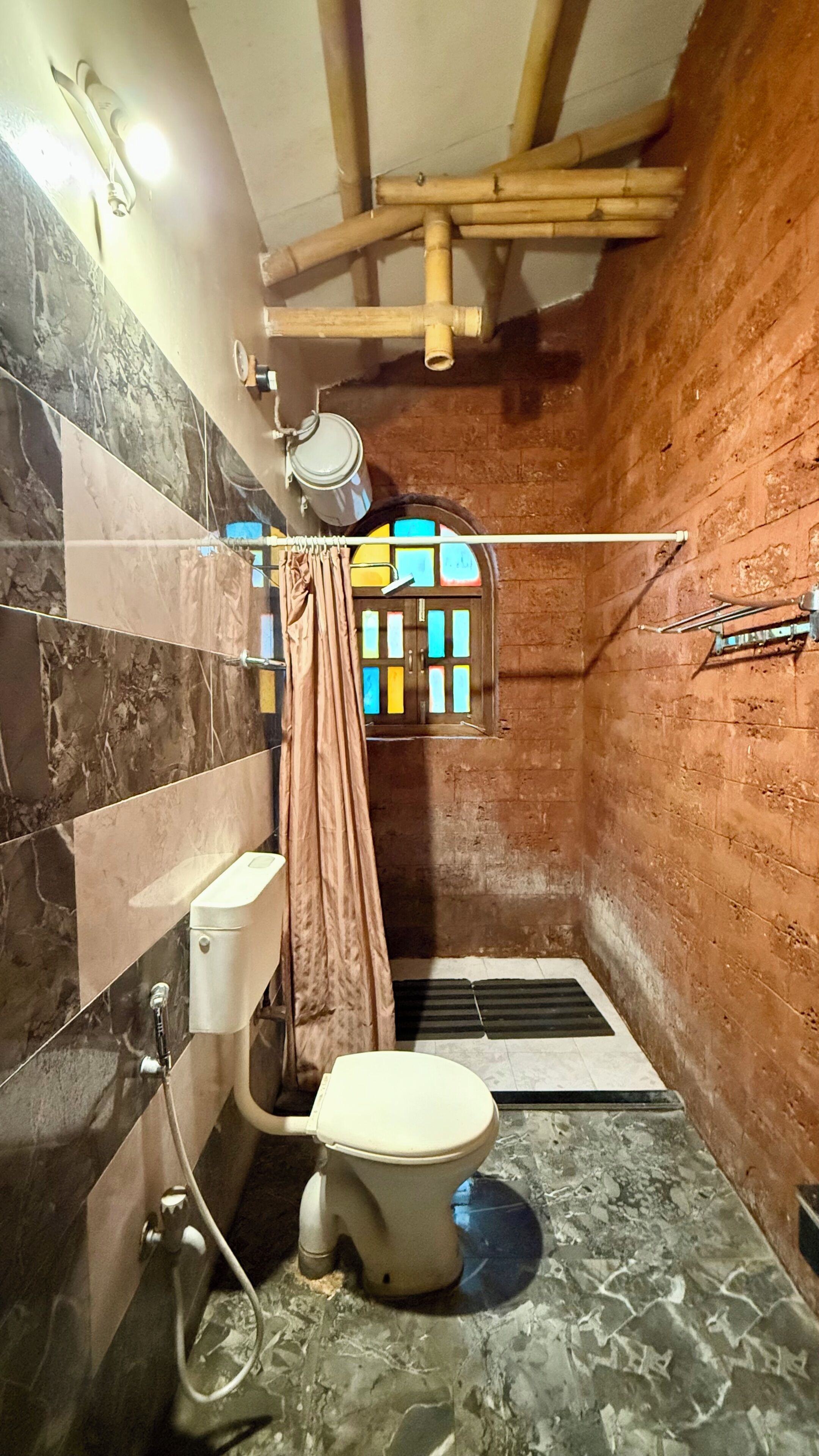 Un baño con inodoro, ducha y una ventana con vidrio de colores.